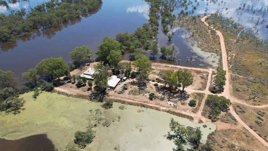 A birds-eye view of a rural property surrounded by water, and with roads cut off by water. There are trees lining the main river