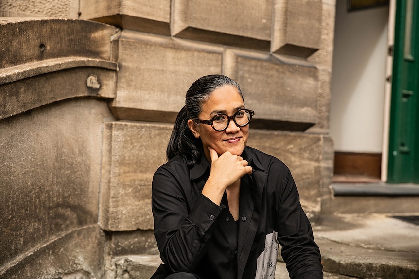 Colour close-up photo of Kylie Kwong sitting on steps in front of sandstone building at the National Art School in Sydney.