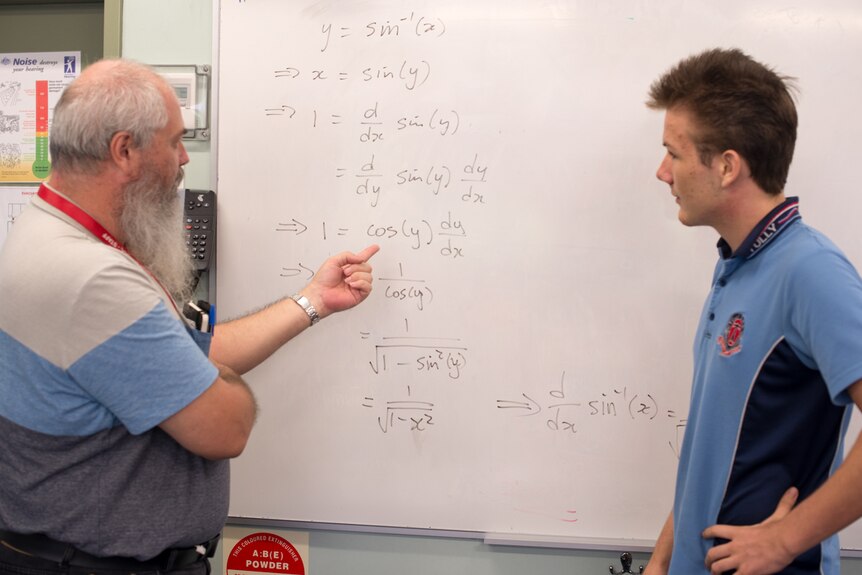 A bearded teacher talks through a complicated mathematical equation with a student.
