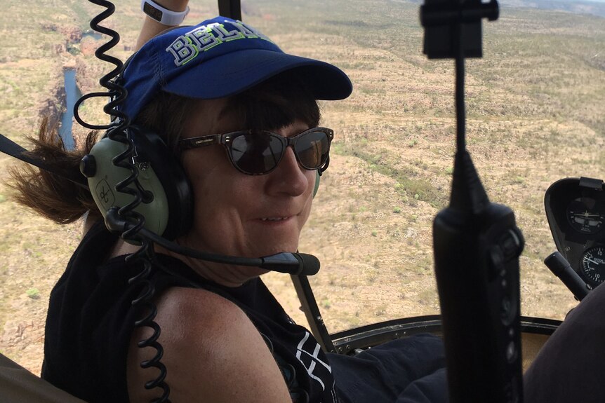 A woman wearing a headset while in a helicopter over an outback area