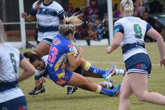 Rachel Warcon tackles a football player on a grass field.