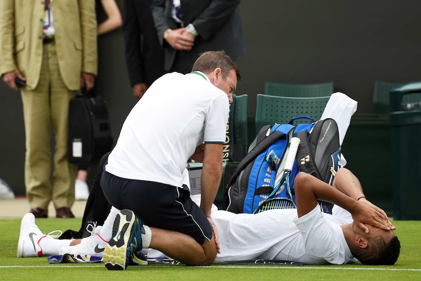 Nick Kyrgios receives medical attention after aggravating his hip injury.