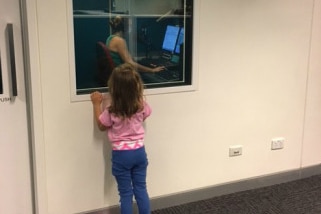 ABC Tropical North lead reporter Mel Maddison reading a news bulletin as her daughter watches on outside the recording booth.