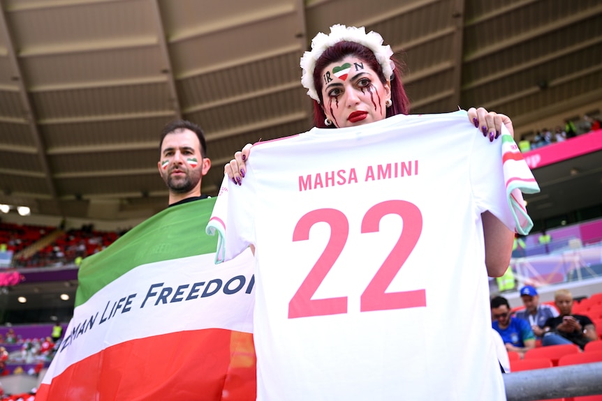 Iran supporters hold up a flag saying women life freedom and a shirt with Mahsa Amini 22 on it