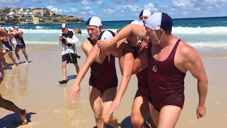 A swimmer is carried by several men in 1938 surf lifesaving uniforms.