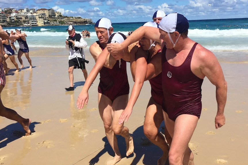 A swimmer is carried by several men in 1938 surf lifesaving uniforms.