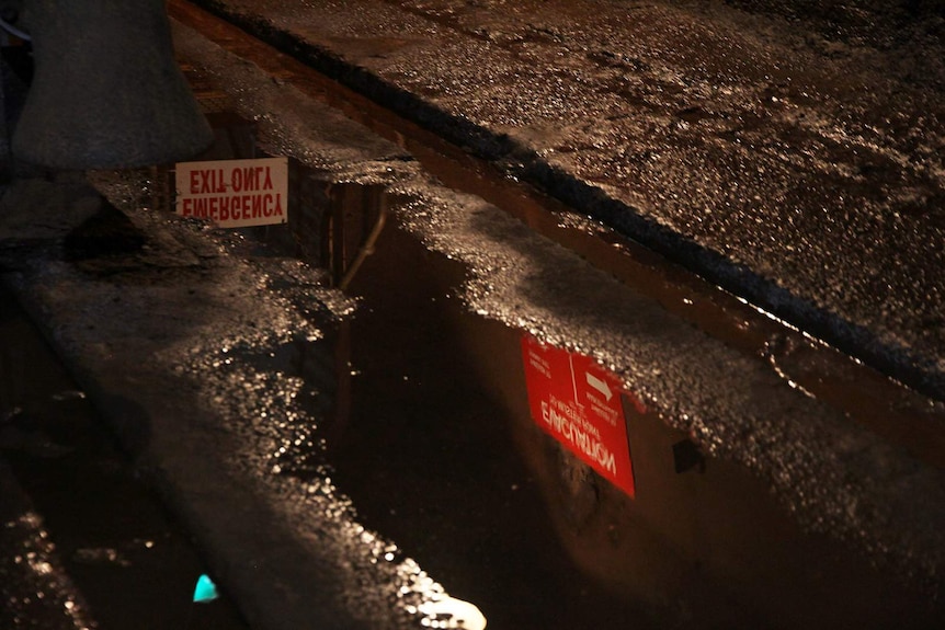 A photo of a puddle in the oil storage tunnels, with two signs visible in the reflection.
