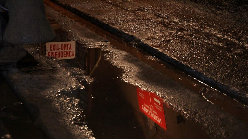 A photo of a puddle in the oil storage tunnels, with two signs visible in the reflection.