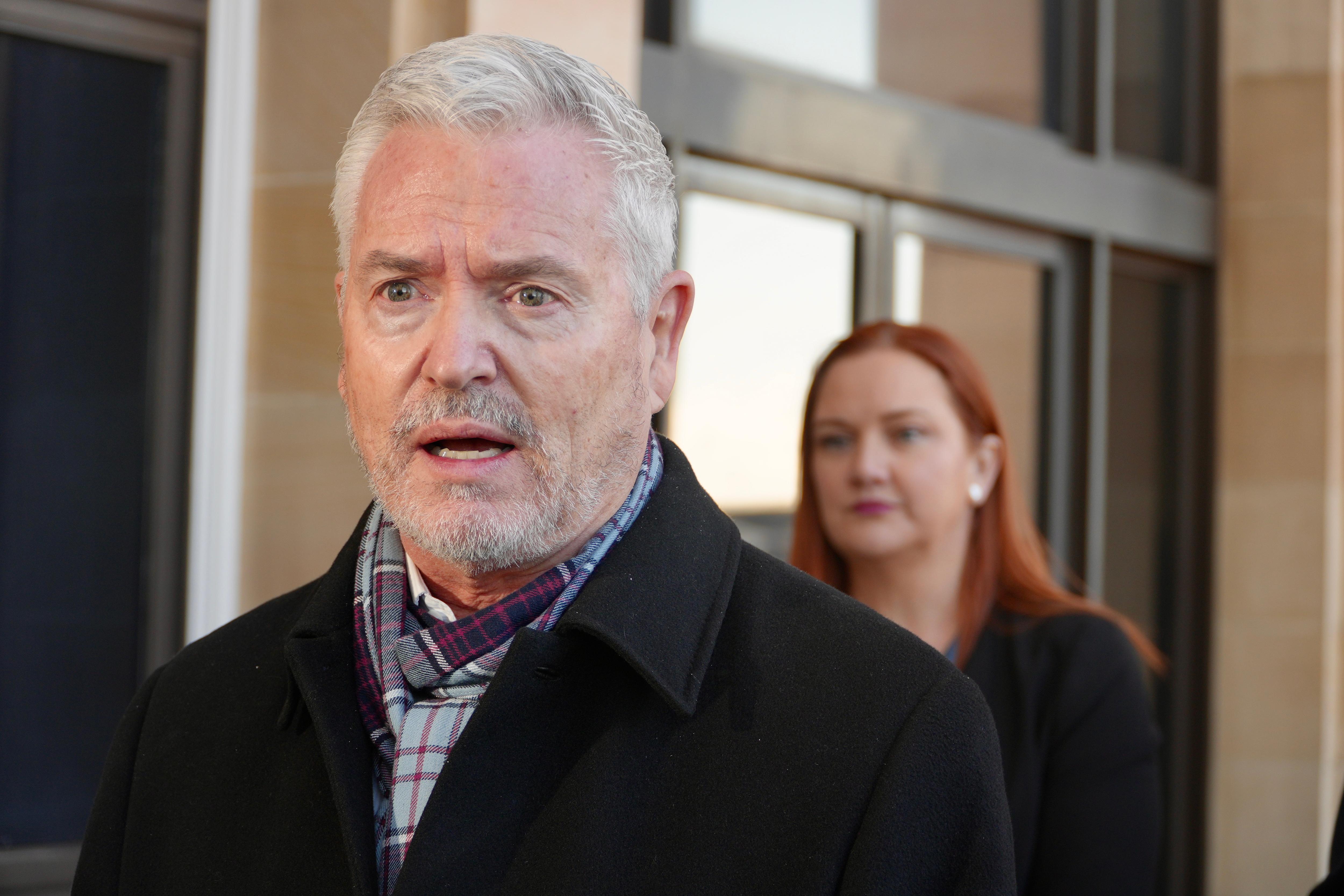Michael Chester wears a black coat and scarf as he addresses a press conference