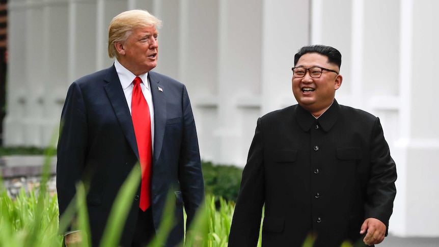 Donald Trump and Kim Jong-un smiling and walking along a grassy pathway.