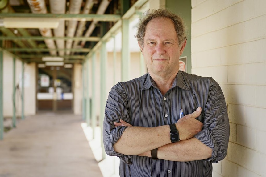 A man with his arms crossed over his chest, standing in an outdoor corridor.