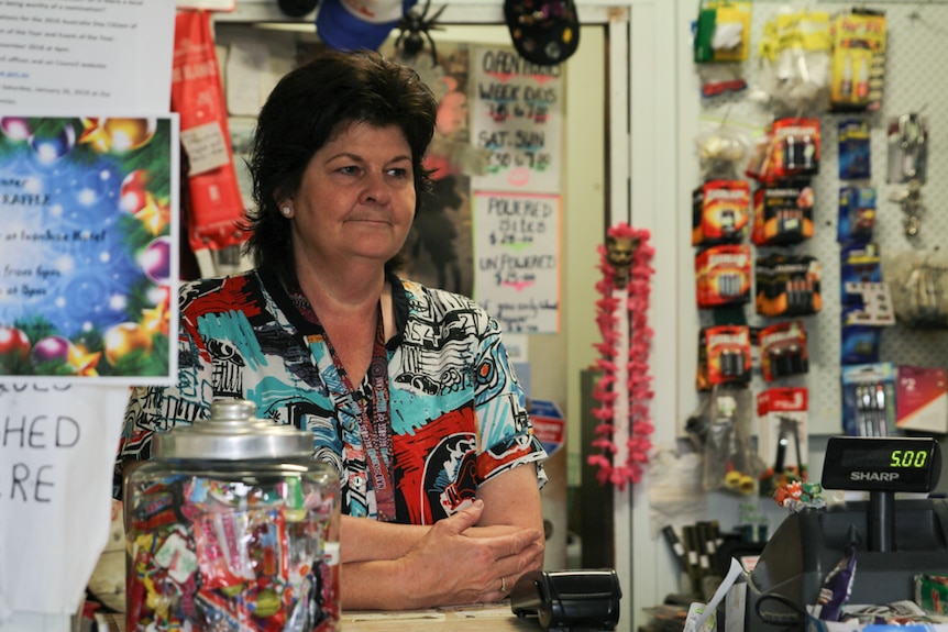 A woman stands behind a counter in a general store.