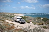 A man and woman look out at the windy beach next to their caravan.