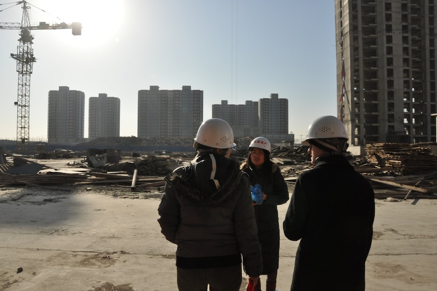Women wearing construction hats stand on an apartment construction site.