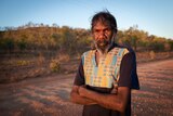 A man stands with arms crossed on a remote dirt road. 