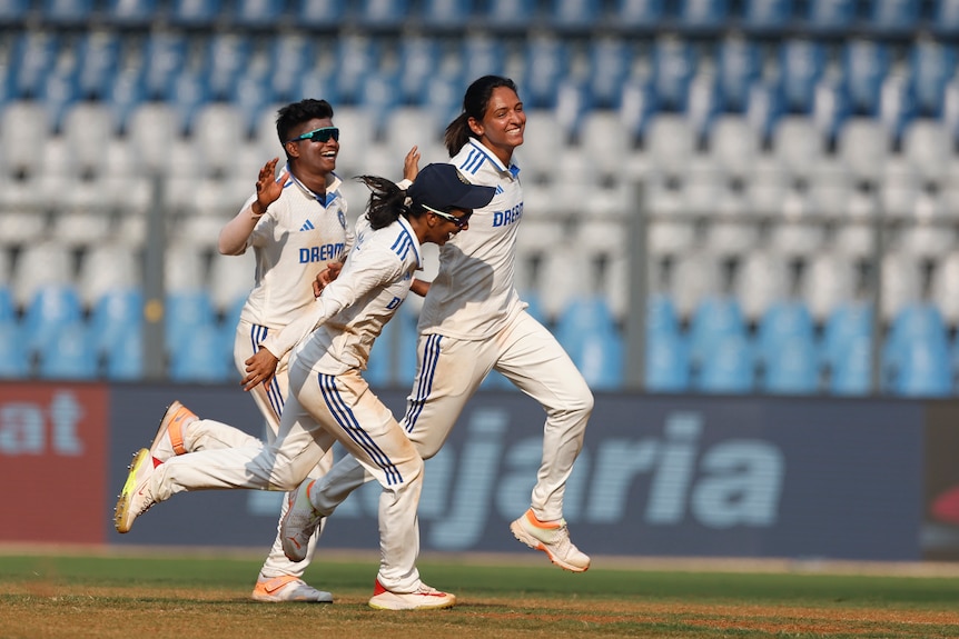 Three Indian players run together with their arms out by their sides as they celebrate a wicket