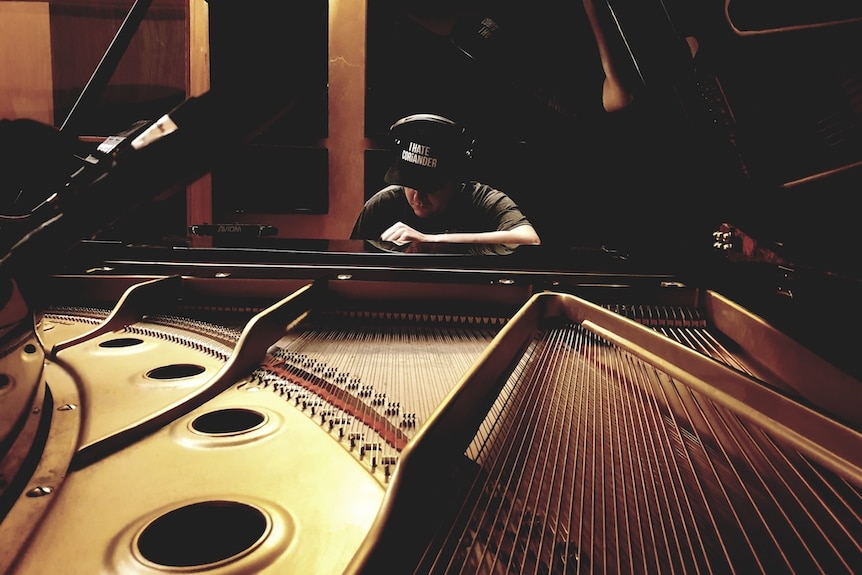 A man sits behind an open grand piano and looks down at the piano keys