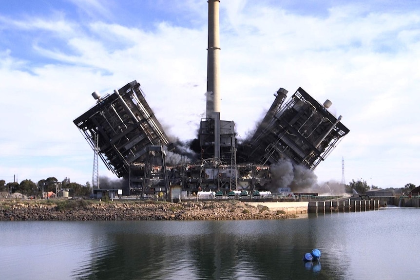 Two large structures are being demolished, falling to either side of a large power station stack.