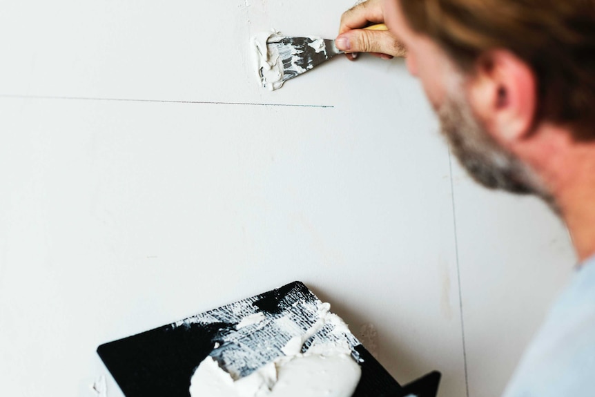 A man paints a wall with white paint to depict the notion of being realistic when planning time for hobbies and personal tasks.