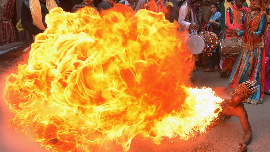 A large ball of flame erupts from the mouth of a fire breather lying on the ground as he performs in a street.