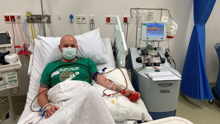 Man wearing green shirt in hospital bed with needles in arms, donating stem cells. 