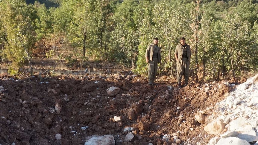 Two fighters stand over the scene of a bomb crater