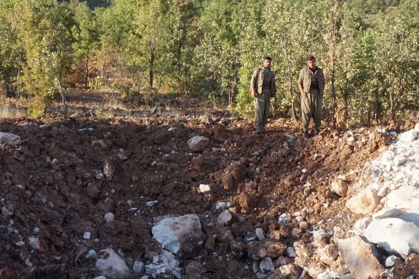 Two fighters stand over the scene of a bomb crater