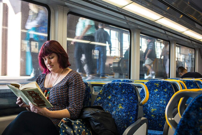 Colour photograph of a woman reading a book in a train carriage.