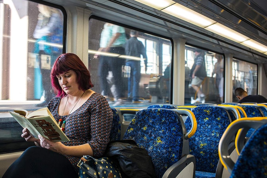 Colour photograph of a woman reading a book in a train carriage.