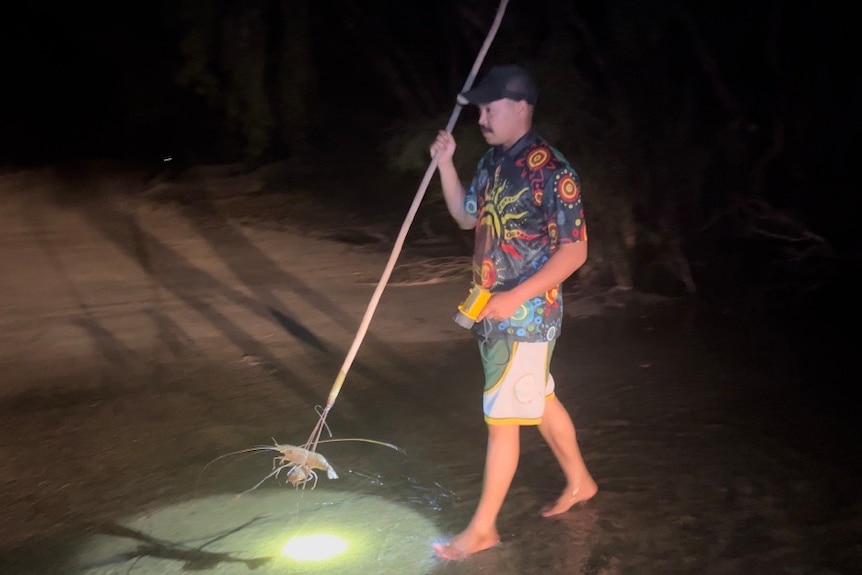 A man holds a torch to illuminate a prawn he has caught at night with a spear