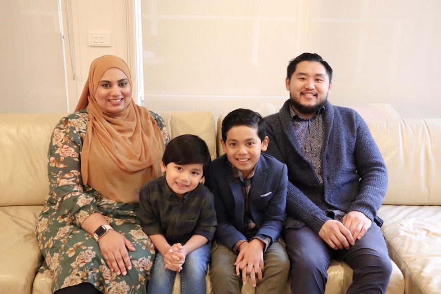 A Chinese man sits next two a Pakistani woman, with two kids in between. 