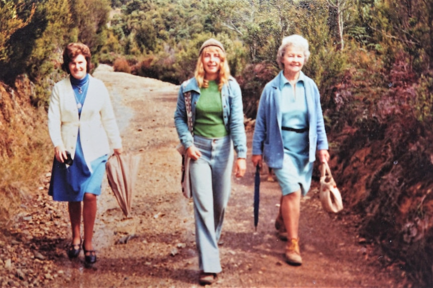 Three women walk along a path in the bush.