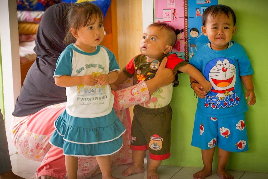 Three small children getting measured against a wall