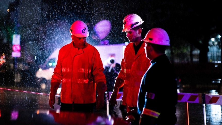 Technicians of Edenor electricity company stand under the rain as they work to fix a generator.