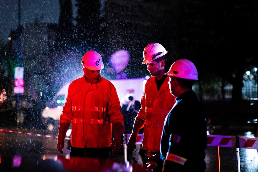 Technicians of Edenor electricity company stand under the rain as they work to fix a generator.