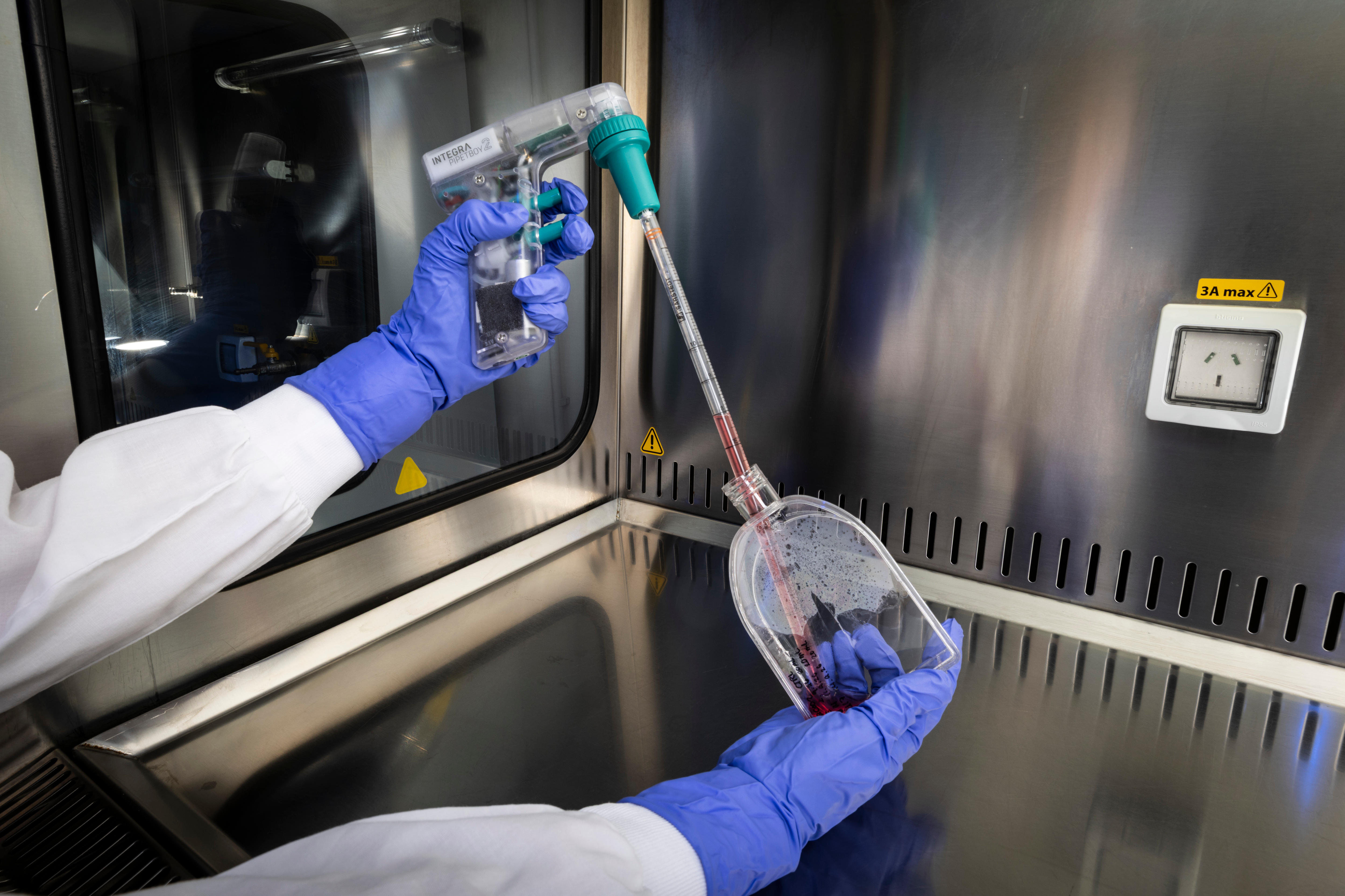A person holds up a plastic container with red liquid being put in it in a lab.
