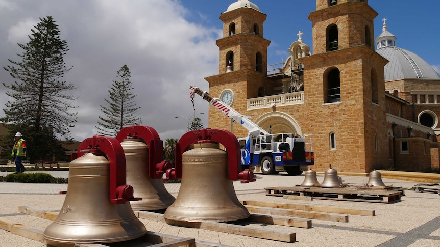 Bells sit on pallets waiting to be lifted into place on the cathedral by a crane in the background.