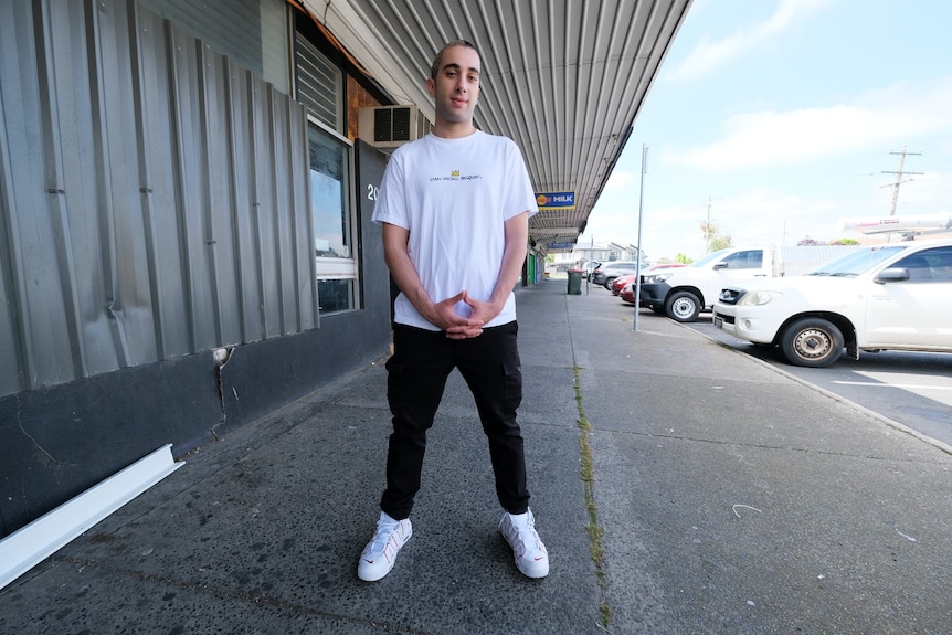 Berat Kaya standing on a footpath with his hands clasped, looking at the camera with a thoughtful expression.