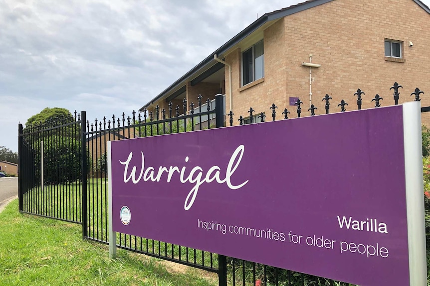 A purple sign with white writing saying Warrigal in front of an aged care home.