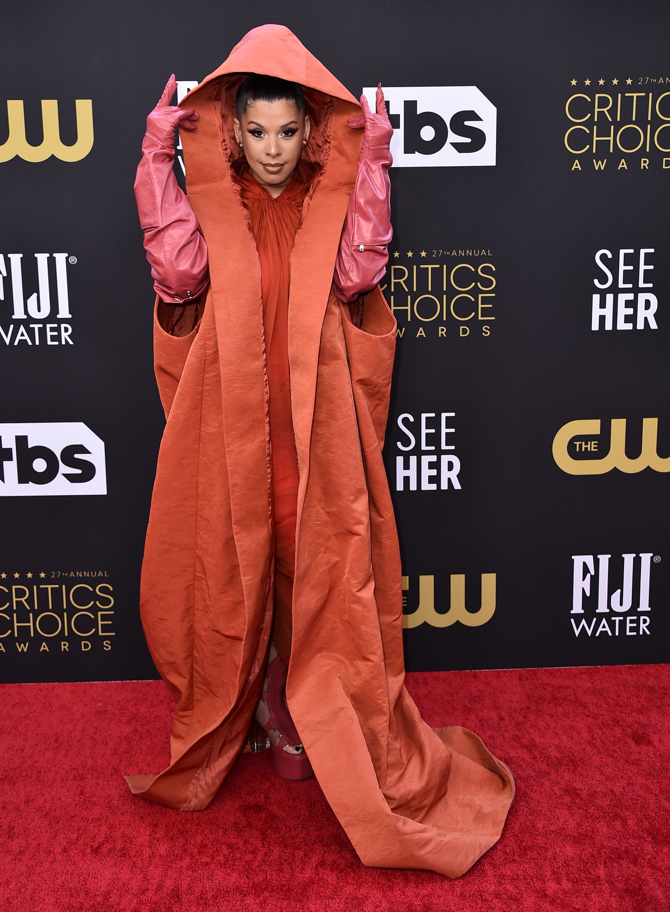 Hailie Sahar wears a hooded gown and gloves on the Critics Choice Awards red carpet.