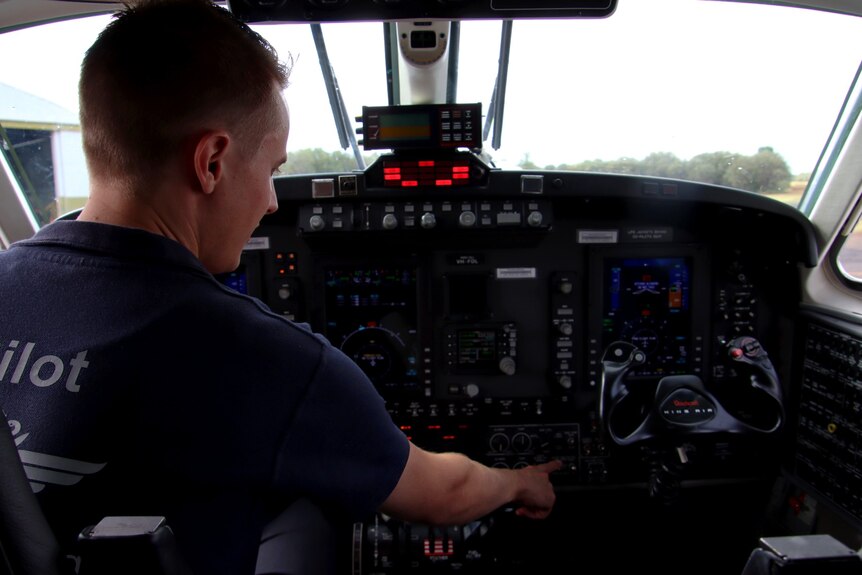 A man is pressing buttons in the cockpit of a small plane. 