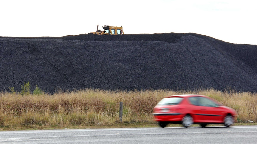 A car drives past a stockpile of coal.