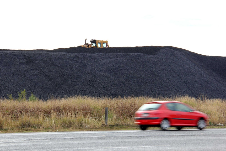 A car drives past a stockpile of coal.