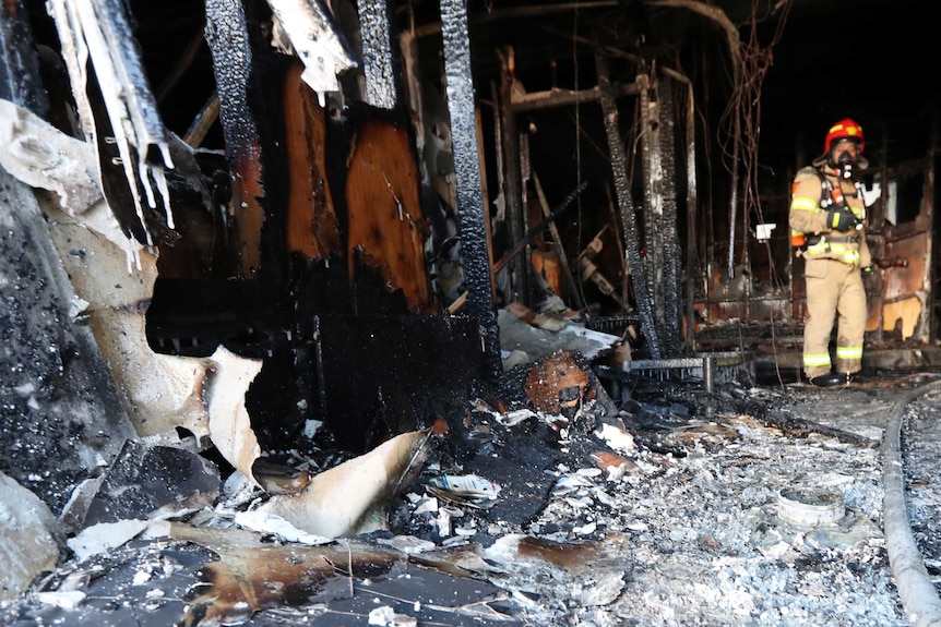 A firefighter inspects a burnt hospital and ash on the ground after a fire in South Korea.