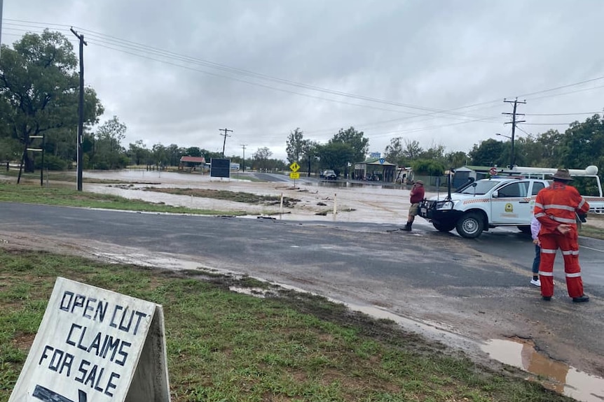 SES volunteers stand next to water over a road.