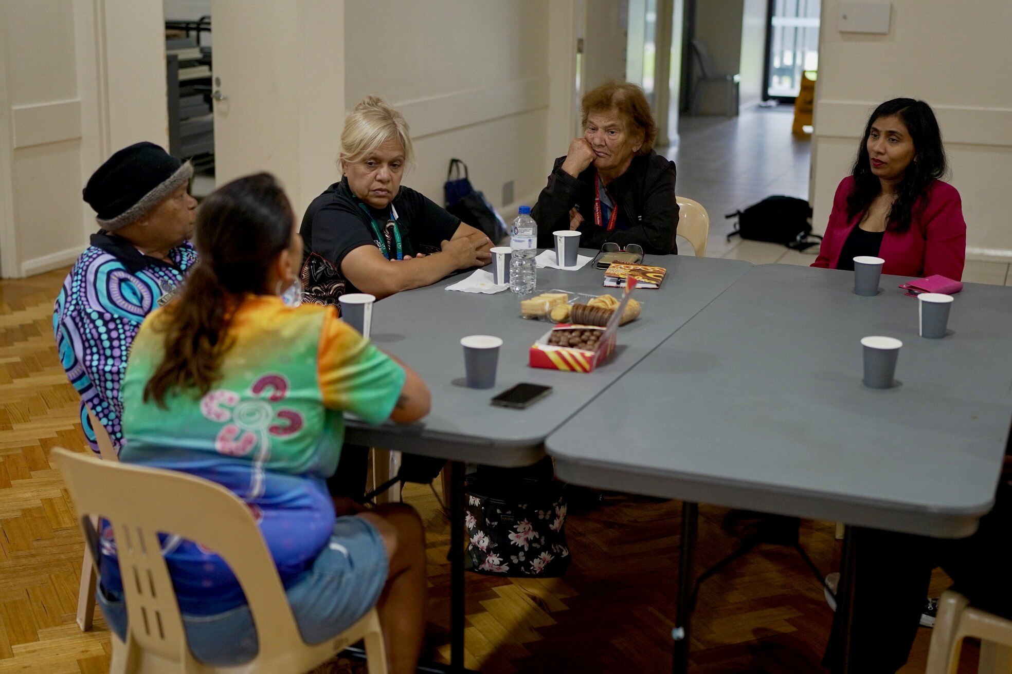 Shenane sits at a table with female Indigenous elders and MP for Swan, Zaneta Mascarenhas.