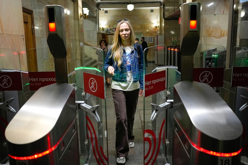A woman in a denim jacket walks through clear ticket barriers inside a subway station in Moscow.