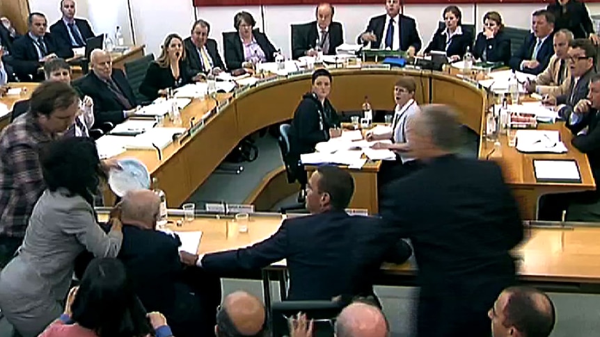 A screen grab shows a man hitting Rupert Murdoch with a foam pie.