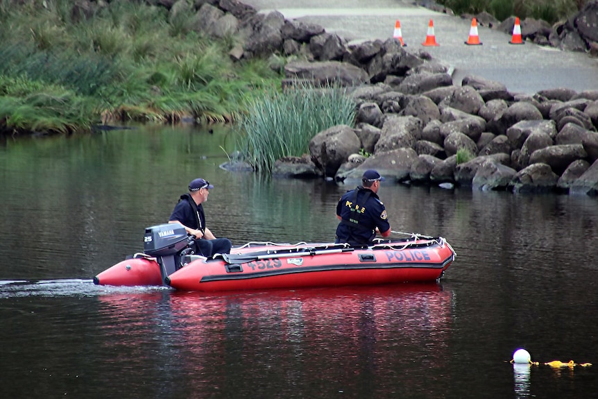 Two police officers on a small boat search a lake area.