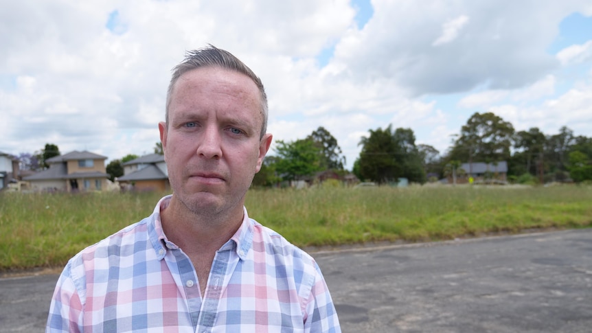 Man stands outside in checkered shirt - he is not smiling